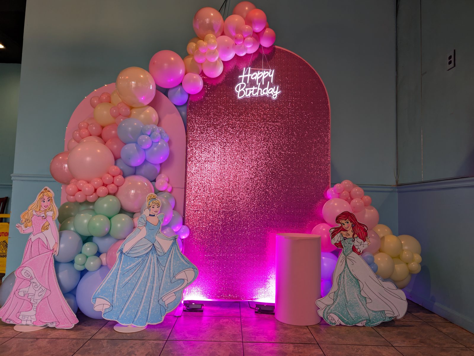 Princess birthday decor with blush balloons, shimmer backdrop, character standees, neon sign, and pink uplighting