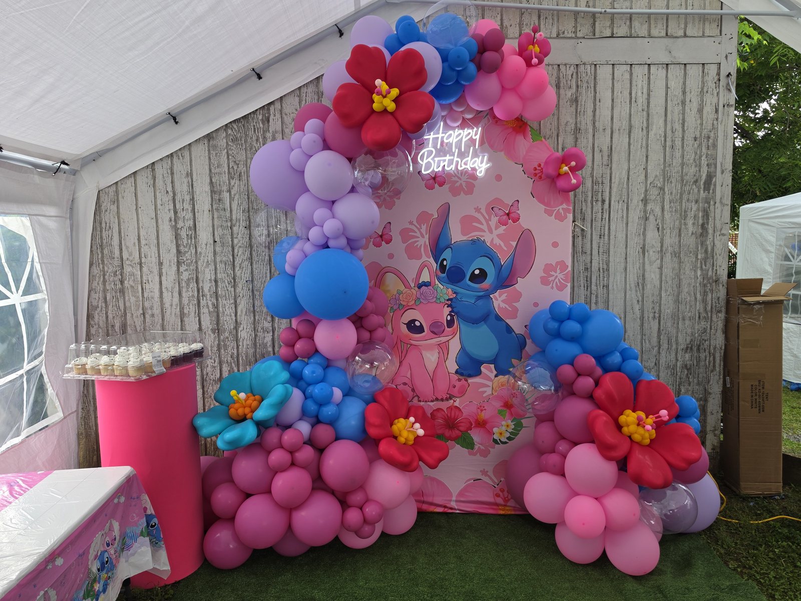 Floral Stitch themed birthday decor with pink and blue balloons, tropical flowers, and custom backdrop