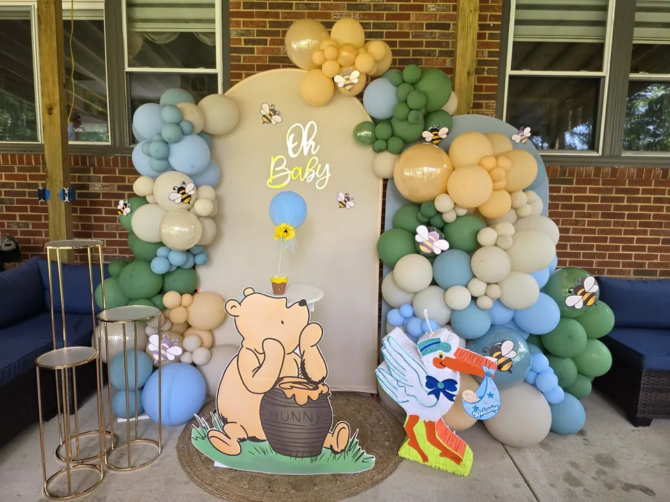 Winnie the Pooh baby shower backdrop with bees, soft balloons, and themed props