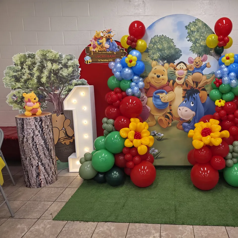 Classic Winnie the Pooh first birthday backdrop with red, yellow, green, and blue balloons